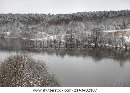 Beautiful river with snow covered bare tree and forest on snowy riverbanks - European winter river landscape