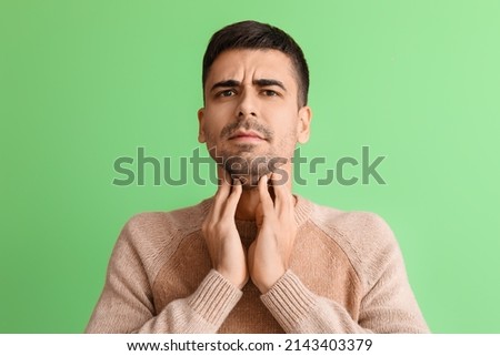 Ill young man with sore throat on green background