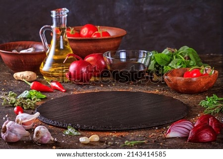 Culinary background with kitchen slate round board, olive oil in a jug and vegetables. Empty space for menu or recipe with selective focus Royalty-Free Stock Photo #2143414585