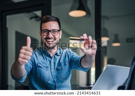 Delighted adult man, giving thumbs up, while showing his credit card to the camera.