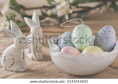Decorative Easter eggs in pastel colors in a white handmade bowl and two wooden Easter bunnies on a wooden table, Easter decoration