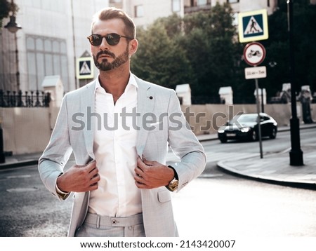 Portrait of handsome confident stylish hipster lambersexual model.Sexy modern man dressed in elegant white suit. Fashion male posing in the street background in Europe city at sunset. In sunglasses Royalty-Free Stock Photo #2143420007