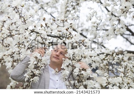 Beautiful smiling man on the background of white flowering magnolia