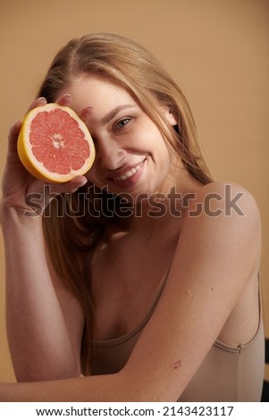 Happy smiling clean skin woman holding red grapefruit near the face with healthy skin and showing vitamins to boost immunity on blue background. Closeup portrait