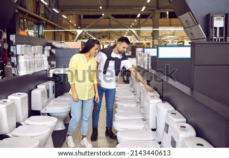 Two customers looking at flush toilets on sale at a modern hardware store or shopping mall. Happy young couple planning renovations in their house and choosing a ceramic toilet bowl for their WC room Royalty-Free Stock Photo #2143440613