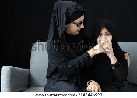 muslim woman or mother giving and feeding fresh milk to her daughter on black background