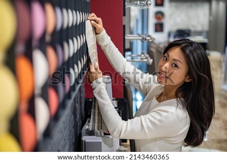 Smiling mixed race woman interior designer choosing textile color and structure for residential apartment decor. Asian female decorator choice fabrics for curtains, pillows, carpets at store showroom