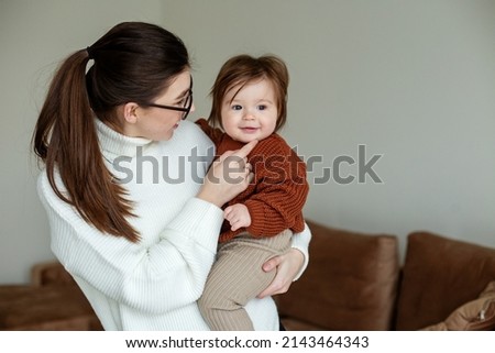 Woman with eyeglasses. Room in beige tones. Babysitter plays with baby.