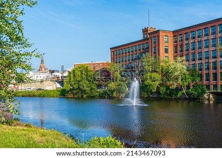Fountain on the Nashua River against the background of a historic cotton factory building with a clock tower in the old industrial park of Nashua. New Hampshire, USA Royalty-Free Stock Photo #2143467093