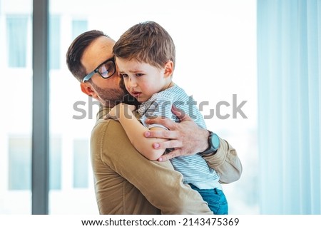 Closeup Sad young blond boy crying on father hands indoor. Man holds son, hugs and comforts. Family love, care and moral support, baby's tears, daddy's arms. Dad consoling crying child