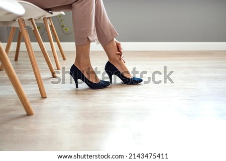 Close up young woman sitting on chair, taking off high heel shoes, massaging tired foot relieving pain ache in office. Exhausted millennial lady feeling feet discomfort, wearing narrow footwear. Royalty-Free Stock Photo #2143475411