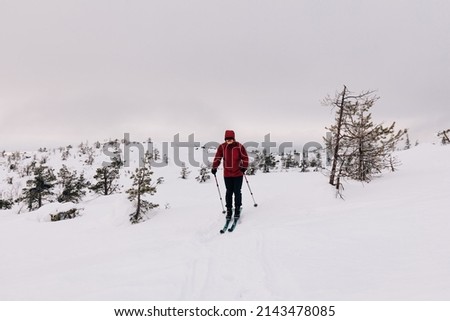 A man rides tourist skis on snowy slopes on a cloudy winter day