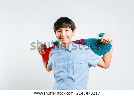 Smart race mix boy kid smiles while holding colorful surf skate or skateboard while standing over a white background. Preteen child in blue shirt, Extreme sports, life energy Concept.