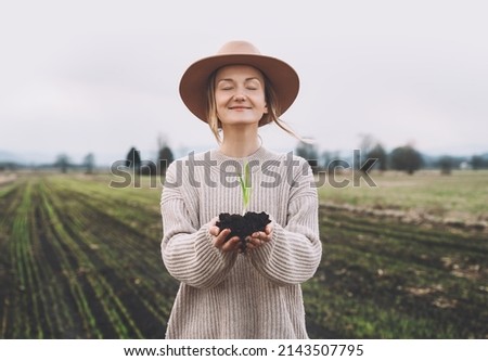 Young plant in hands in background of agricultural field area. Woman holding in hands green sprout seedling on black soil. Concept of Earth day, organic gardening, ecology, sustainable life. Royalty-Free Stock Photo #2143507795