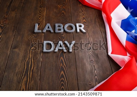 words labor day laid with silver metal letters on wooden surface with crumpled USA flag on left side in linear perspective