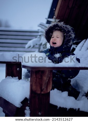 Little boy crying on the porch of a snow-covered wooden house
