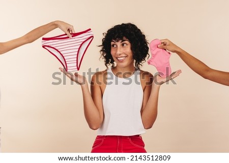 Weighing my sanitary options. Happy young woman making a choice between a period panty and a reusable pad. Cheerful woman choosing the right non-disposable product for her feminine hygiene.