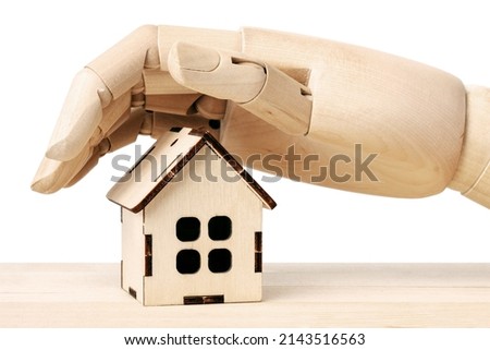 Wooden doll's hand covers protecting from above a wooden toy house isolated on a white background. Insurance protection concept.