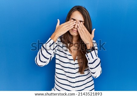 Young hispanic woman standing over blue isolated background rubbing eyes for fatigue and headache, sleepy and tired expression. vision problem 