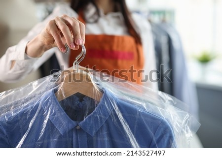 Administrator at dry cleaners keeps clean clothes on hangers in bag Royalty-Free Stock Photo #2143527497