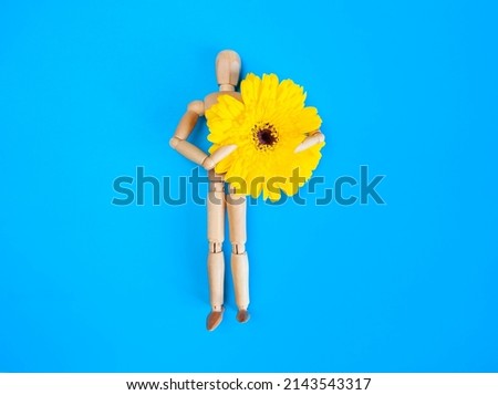 wooden mannequin holding blossoming yellow gerbera flower