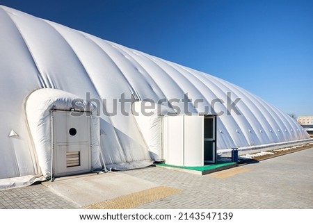 Inflatable air dome stadium. Inflated Tennis air dome or Tennis bubble arena entrance door into structure equipped with airlock either two sets of parallel doors or a revolving door or both. Royalty-Free Stock Photo #2143547139