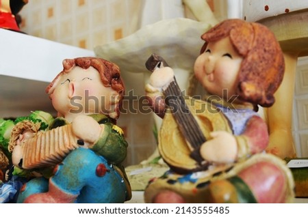 Souvenirs toys and vintage resin boy doll and retro girl figurine playing accordion and harp on shelf for show in local gifts shop for thai people travelers visit and select buy in Bangkok, Thailand