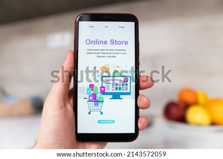Smart phone online shopping in young man's hand. Desk with coffee in the background. Buy clothing accessories shoes from e-commerce website
