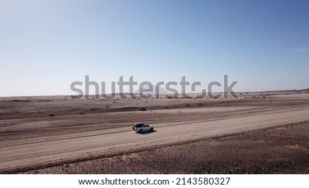 Car driving on gravel road in aerial desert. Sandy landscape, nobody. Wildlife, mountains. Nature in Africa. Highway. SUV white automobile vehicle. Royalty-Free Stock Photo #2143580327