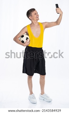 fitness man with lean body, sportsman in black shorts and yellow t-shirt holding soccer ball and phone, selfie. The concept of sports motivation for training.