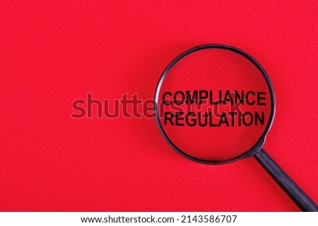 Magnifying glass with text Compliance Regulation on bright red surface.