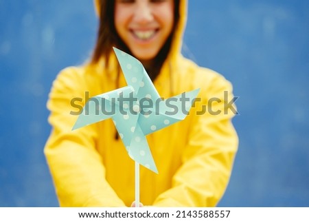 Cropped detail of woman holding a blue windmill in yellow background. Vertical selective focus of windmill meaning environmental concern about wind energies. Renewable energies concept.