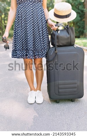 Photo of woman's legs wearing white shoes and summer polka dot dress with suitcase and bag and hat on suitcase. Travel concept. Summer. Adventures and journey 