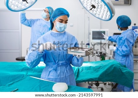 Female surgeon in surgical uniform taking surgical instruments at operating room. Young woman doctor in hospital operation theater Royalty-Free Stock Photo #2143597991