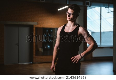 Handsome friendly athlete or personal trainer in gym. Young sporty man smiling standing on fitness club background