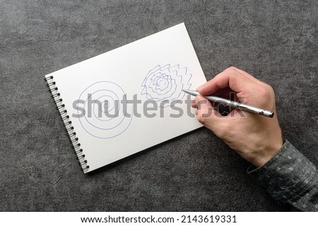 A man with trembling hands is trying to repeat the spiral drawing in a notebook. Test for essential tremor and parkinson's disease. Royalty-Free Stock Photo #2143619331