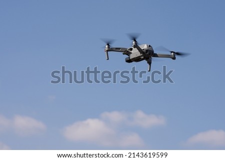 A modern quadcopter with a high resolution camera hovering in the air. A compact gray RC drone takes aerial photo or video footage from the air. Gadget in flight against the blue sky. Drone control.