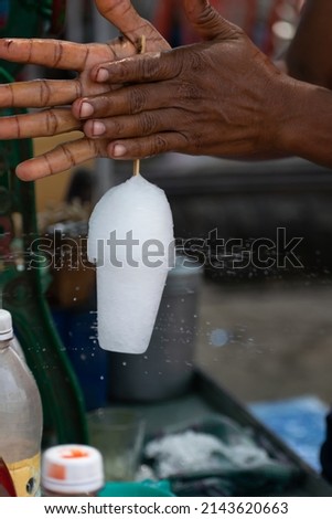 Picture of hand of a person, worker, labour, vendor churning ice candy. Crushed ice, summer, refreshment, cold drink, chuski, sugar syrup, kala khatta, glass, cool, colorful, tasty, kids, ice concept.
