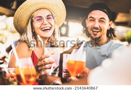 Trendy couple having fun drinking fancy cocktails at beach party - Summer joy and genuine life style concept with young people at festival happy hour - Warm contrast filter with focus on left woman Royalty-Free Stock Photo #2143640867