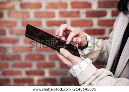 unrecognizable asian business woman in city using mobile phone.Bricks background