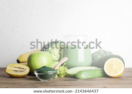 green smoothie in glass, spirulina powder, vegetables and fruits on wooden background. healthy, raw, vegan diet concept. copy space