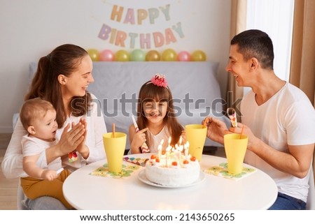 Image of smiling delighted family sitting at the table and celebrating birthday, parents and children talking and laughing, celebrating festive event.
