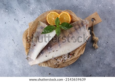 Seafood. Raw halibut fillet with lemon, spices, salt and basil on a wooden board on a light grey background. White fish. Flatlay, top view. Background image, copy space