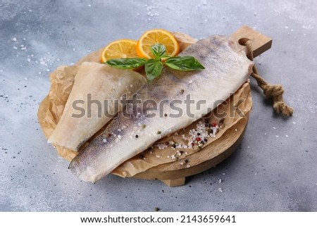 Seafood. Raw halibut fillet with lemon, spices, salt and basil on a wooden board on a light grey background. White fish. Background image, copy space