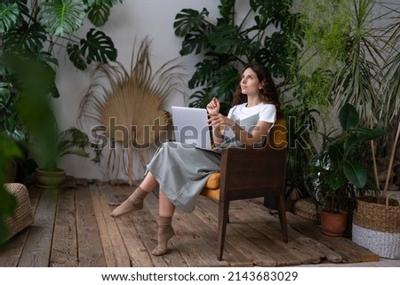 Florist girl entrepreneur planning new indoor garden sit with laptop in home orangery working remotely. Young freelancer event designer or decorator businesswoman create plan of decoration for client Royalty-Free Stock Photo #2143683029