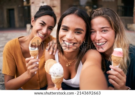 Three young smiling hipster women taking selfie outdoors in summer clothes eating ice cream. Female 20s friends having fun and enjoying summer vibes together. Holiday vacation time Royalty-Free Stock Photo #2143692663