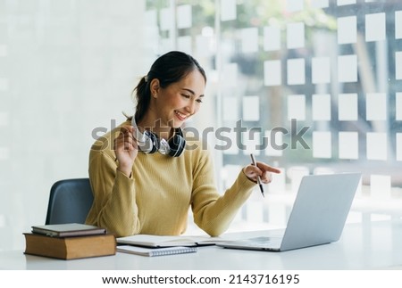 Smiling Asian young female using headset looking at laptop screen listen and learning online courses. Happy asian business woman with headphones video call for customer service.