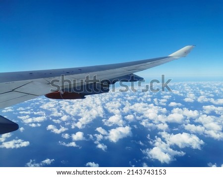 View from the porthole on the wing of an airplane with a red aircraft engine flying in the morning over beautiful white clouds and the Mediterranean Sea.