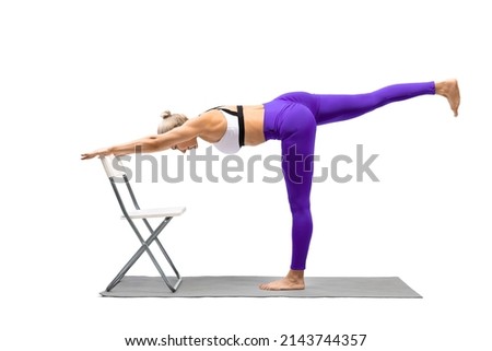 Iyengar yoga balance. Fit caucasian woman in purple leggings practice warrior pose III using a chair, Virabhadrasana III, isolated on white. Advertising, rehab, mental health, exercise, female health