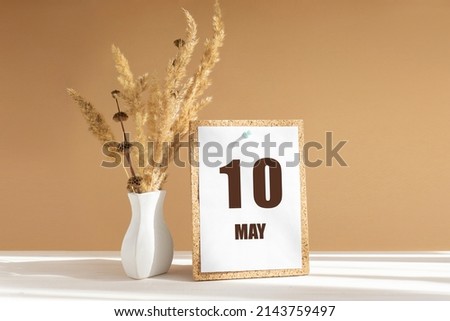 may 10. 10th day of month, calendar date.White vase with dried flowers on desktop in rays of sunlight on white-beige background. Concept of day of year, time planner, spring month.
